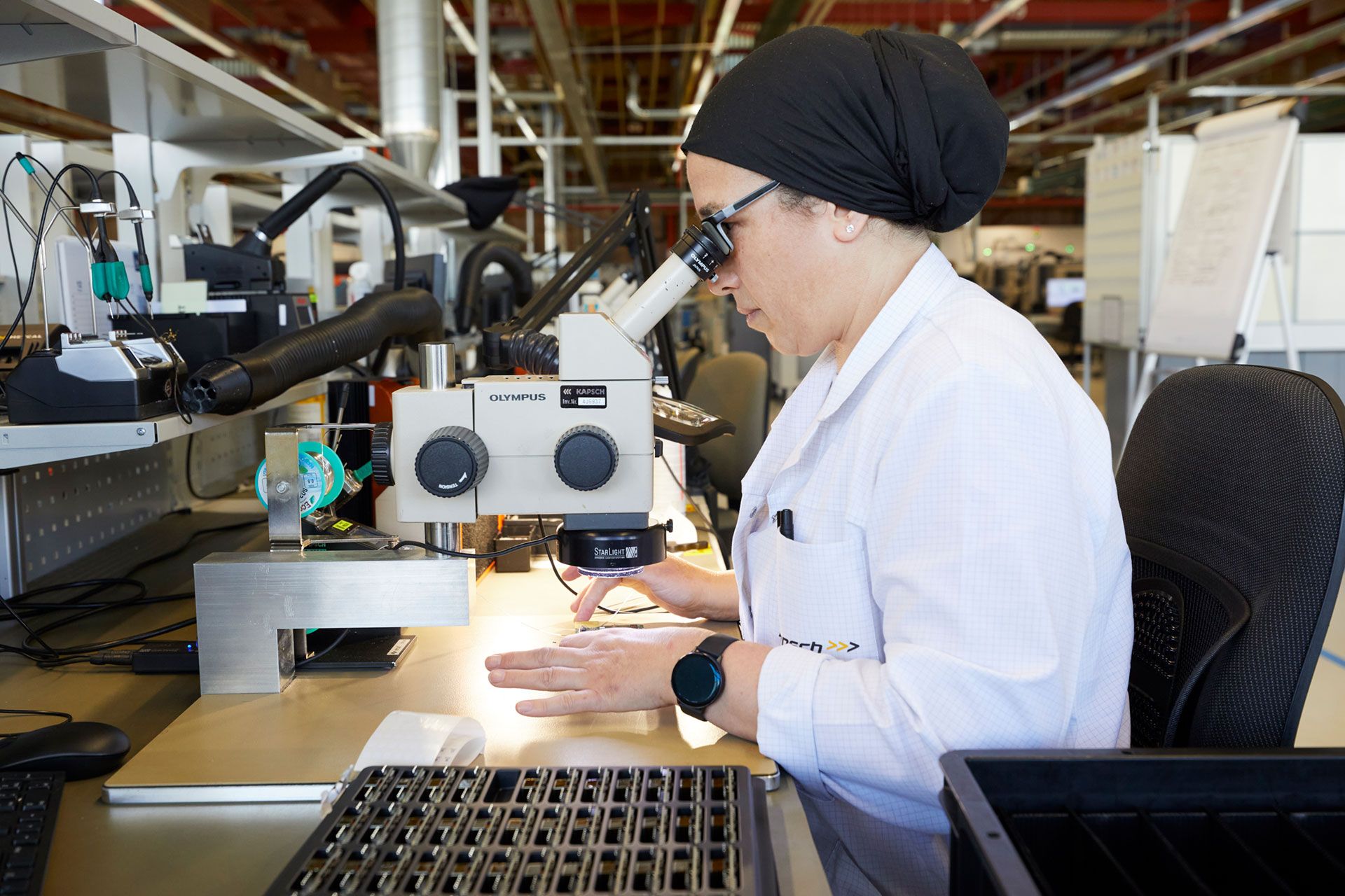Una técnica de Kapsch Components observando a través de un microscopio en un laboratorio.