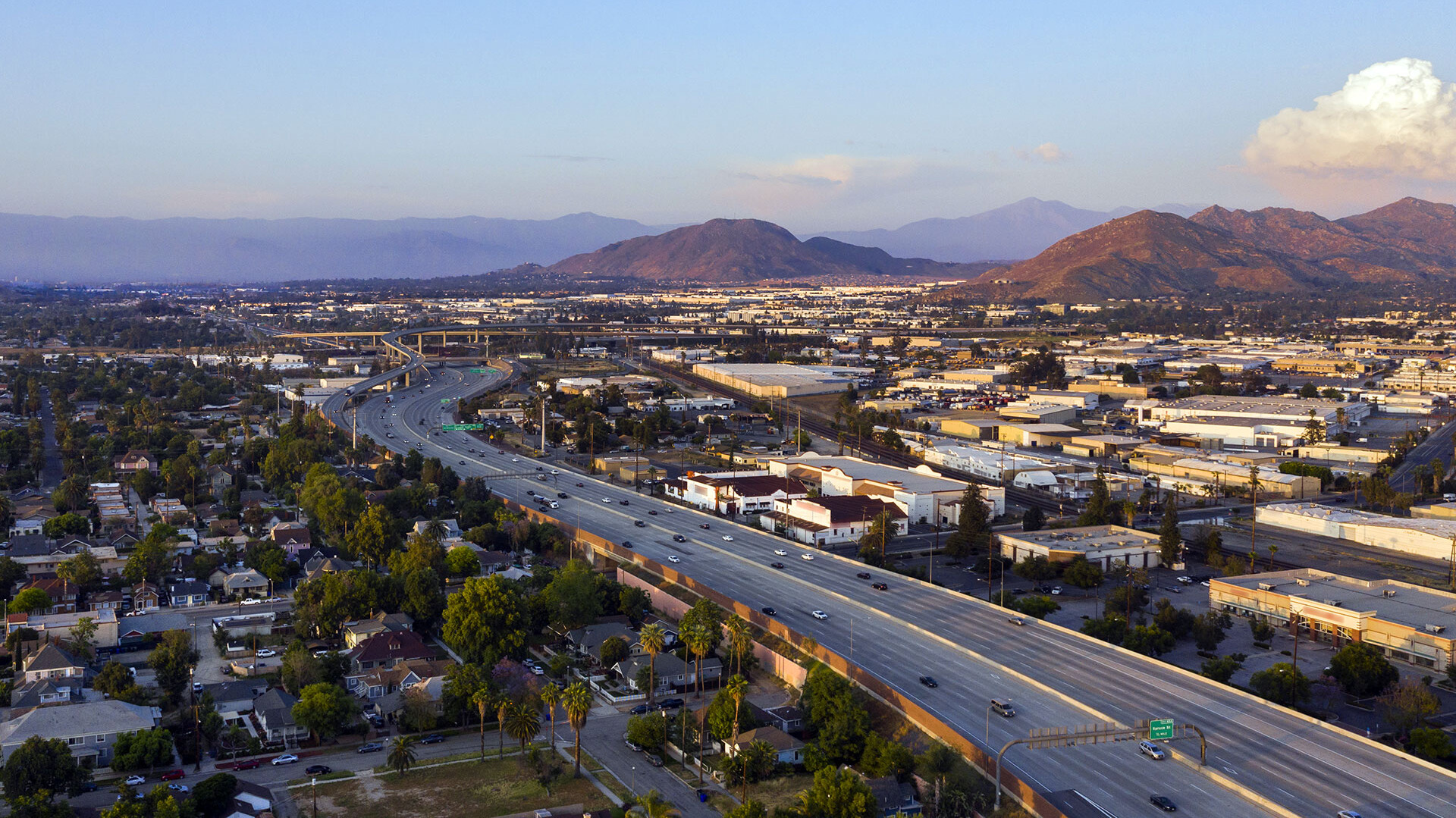 Luftaufnahme einer Autobahn in einer Stadt mit umgebenden Gebäuden und Bergen im Hintergrund.