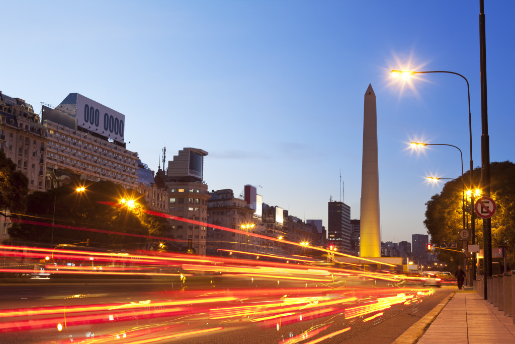 Eine belebte Stadtstraße mit einem hohen Turm und Straßenlaternen, die die nächtliche Umgebung beleuchten, im Kontext der Kapsch Verkehrsintelligenz-Lösungen zur Optimierung des Verkehrsflusses.
